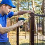 property territory fencing - man screws metal fence panel